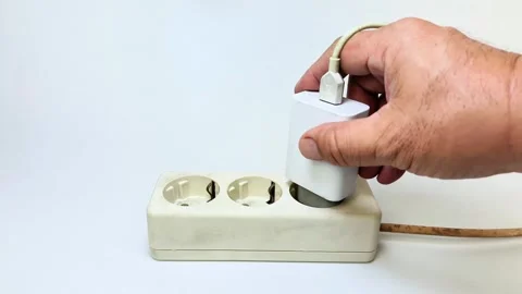 A man's hand trying to plug a cell phone charger into an electrical socket .. Stock Footage 338520662