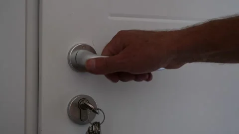 Mans hand turning silver door handle with key in lock on white door Vidéo 343827743