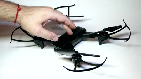 A man's hand turns a small black drone on and off on a white background Stock Footage 342256976