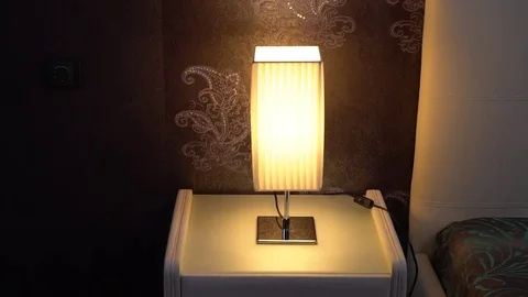 A man's hand turns on table light on a bedside table. 스톡 동영상 75687563