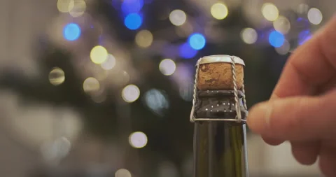 Man's hand unscrews a muzzle from a bottle of champagne standing in front of a Stock Footage 231593729