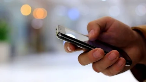 A man's hand uses black smartphone on the background walking people and bokeh Stock Footage 84752194
