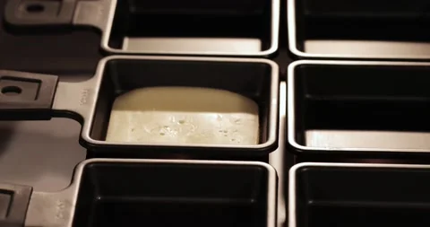 A man's hand using kitchen tongs puts cheese into raclette molds Stock Footage 179026436