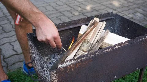 A mans hand is using matches to start a fire in a grill for barbeque Stock Photos