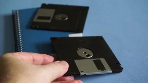 Man's hand using an old floppy disk as a bookmark on a notebook, concept of Stock Footage 340118456