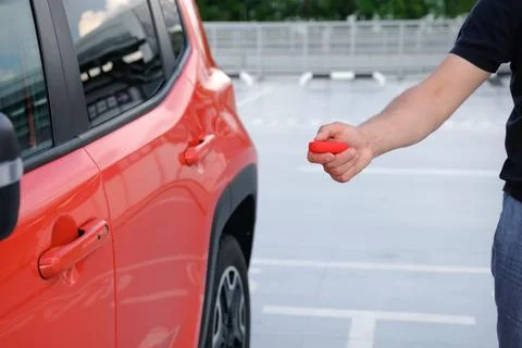 A mans hand using a remote control key to open a car parked in a parking lot Foto stock