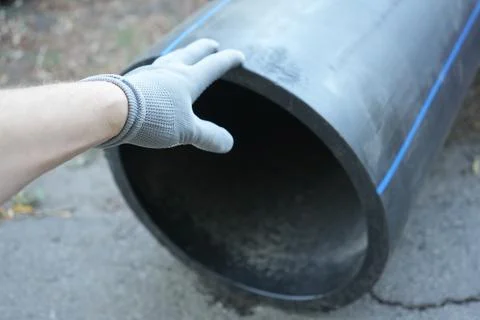 A mans hand wearing a gray work glove slaps a large-diameter black plastic pipe Foto stock