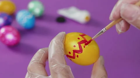 A man's hand, wearing a transparent glove, draws red dots on a yellow Easter egg Stock Footage 174691137