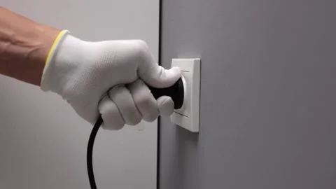 Man's hand in a white glove inserts black wire electrical appliance into socket Stock Footage 267358879