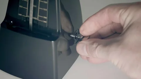A man's hand winds the spring of a new, modern, shiny, black metronome Stock Footage 297773931