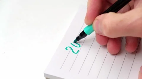 Man's hand writes the numbers of 2023 with a green felt-tip pen in a notebook. Stock Footage 196872452