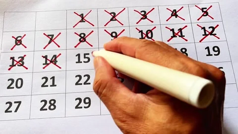 A man's hand writes out all the days on a paper calendar using a red pen Stock Footage 328571906