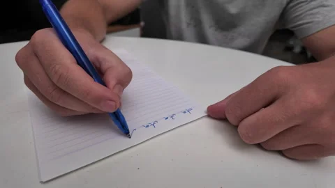 A man's hand writes text with a blue pen on a sheet of notebook paper. Stock Footage 332204288