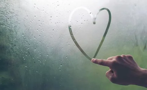 A man's hand is writing a heart-shaped glass window during a rain. Foto stock