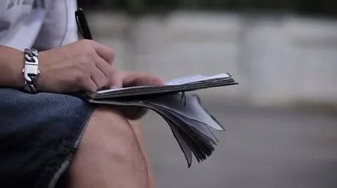 Man's Hand Writing in a Notebook on His Lap in the Street Stock Footage 66550948