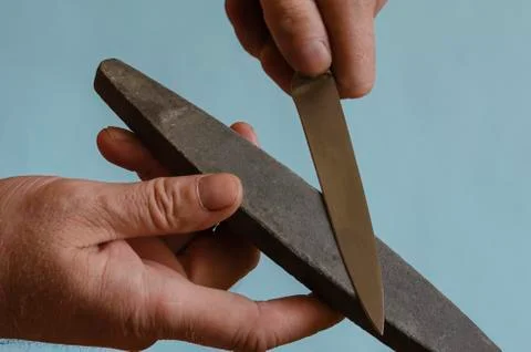 Man's hands are sharpening a small knife on a grindstone. Stock Photos