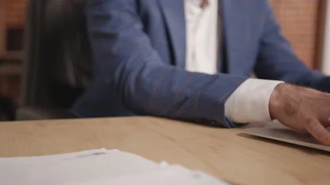 Man's hands are typing something on a laptop then someone gives sheets of paper Stockbeeldmateriaal 191884330