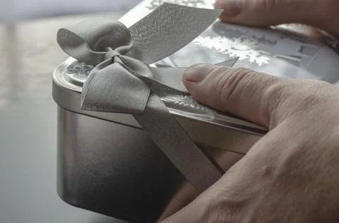 Man's hands banging Large rectangular metal gray gift box with ribbon. Stockfoto's