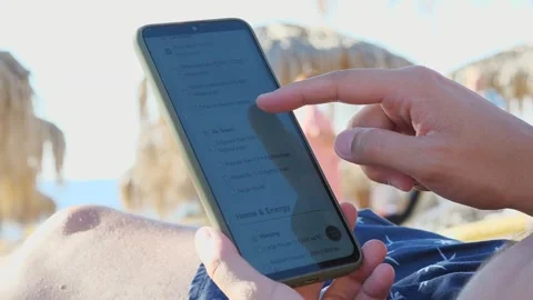 A mans hands at the beach interact with an ecological calculator, selecting 스톡 동영상 318580841