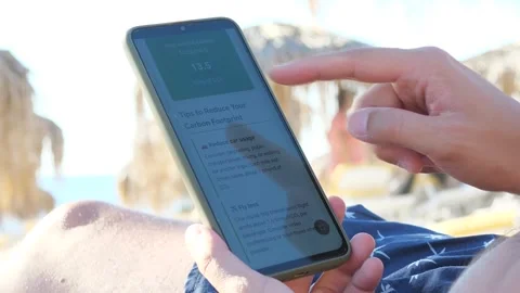 A mans hands on a beach use a smartphone application to calculate carbon Stock Footage 318296876