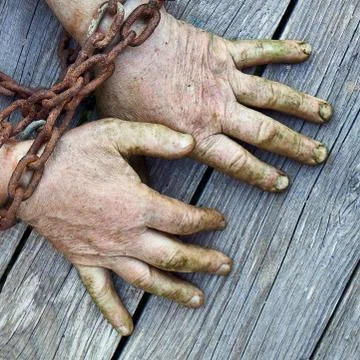 Man's hands chained with old rusty thick chain on the wooden boards Stock Photos