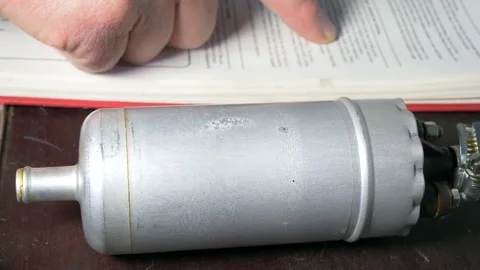 Man’s hands checking a workshop manual with a vehicle fuel pump nearby. Video stock 131919466