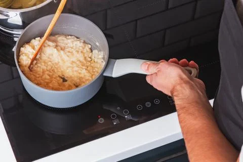 Man's hands close-up stirring risotto in a pot with wooden spatula. Stock Photos