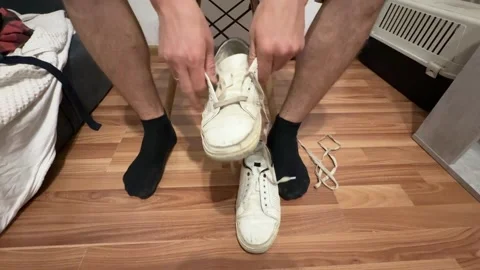 Man's hands close-up threading shoelaces into white sneakers on wooden floor Stock Footage 337338892