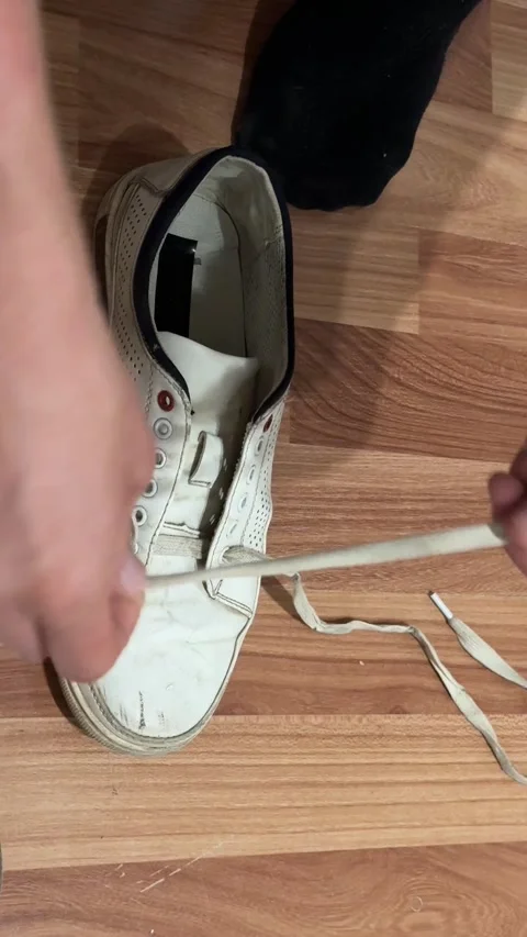 Man's hands close-up threading shoelaces into white sneakers on wooden floor Stock Footage 337354987