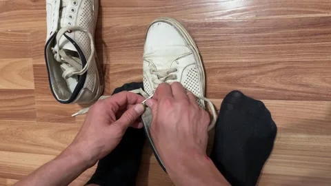 Man's hands close-up threading shoelaces into white sneakers on wooden floor Stock Footage 337414466