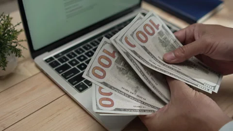 Man's hands counting US hundred-dollar bills over a laptop Stock Footage 346770911