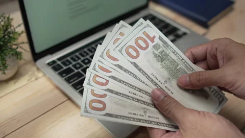 Man's hands counting US hundred-dollar bills over a laptop Stock Footage 346771039