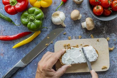 Man's hands cutting bread with cream cheese on wooden cutting board Stock Photos