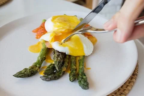 Man's hands cutting poached egg with hollandaise sauce and salmon over asparagus Stock Photos