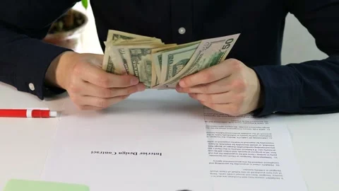A mans hands in a dark casual shirt count cash while an interior design contract Stock Footage 316765960