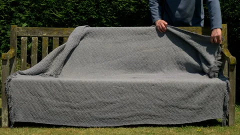 Man’s hands draping a wet rug over a garden bench, to dry off in the sun. Stock Footage 243745784