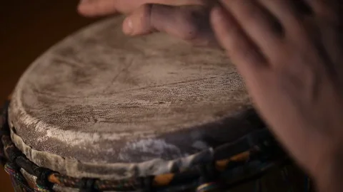 Man's hands drumming out a beat on an African skin-covered hand drum. Stockbeeldmateriaal 74521502