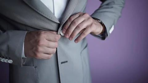 Man's hands fasten buttons on grey classic jacket against purple wall. Stock Footage 200524601