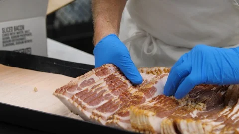 Mans hands in gloves are placing raw bacon slices into the pan close up shot 库存影片 104973586