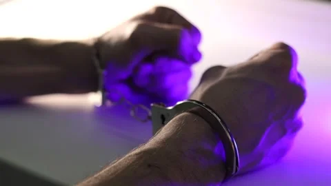 A mans hands handcuffed over a table with police car lights. Stock Footage 329583359