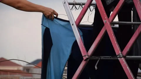 Man's hands hanging simple clothes on steel drying rack on rooftop in Indones Stock Footage 312057612