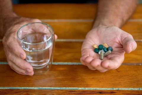 Mans hands hold different tablets and a glass of water Stock Photos