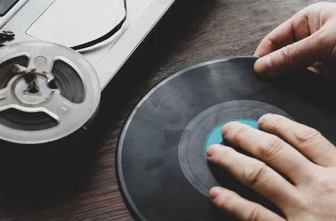 A man's hands hold the record on the table. A laptop computer and an old reel Stock Photos