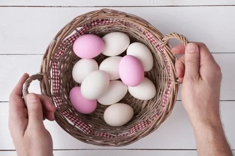 Man's hands holding a basket with Easter eggs on white planks Stock Photos