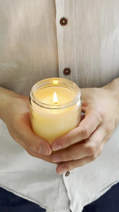 Man's hands holding burning candle in glass jar, decorative container candle Stock Footage 242500565