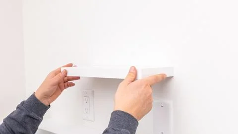 Mans hands holding white rectangular shelf plank against white wall near Stock Photos