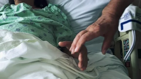 Man's hands holding woman's hands as she lays down in hospital bed Stock Footage