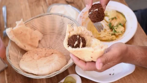 Man's hands holds pita bread with hummus, falafel and slices of cucumbers Stockbeeldmateriaal 184841591