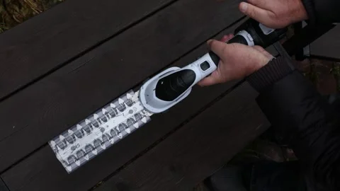 Mans hands inserting battery into cordless hedge trimmer and removing blade Stock Footage 326964390