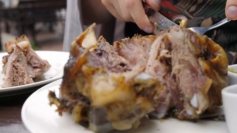 Man's hands with a knife and a fork cuts a pork knuckle and puts it on a plate Stock Footage 115084696